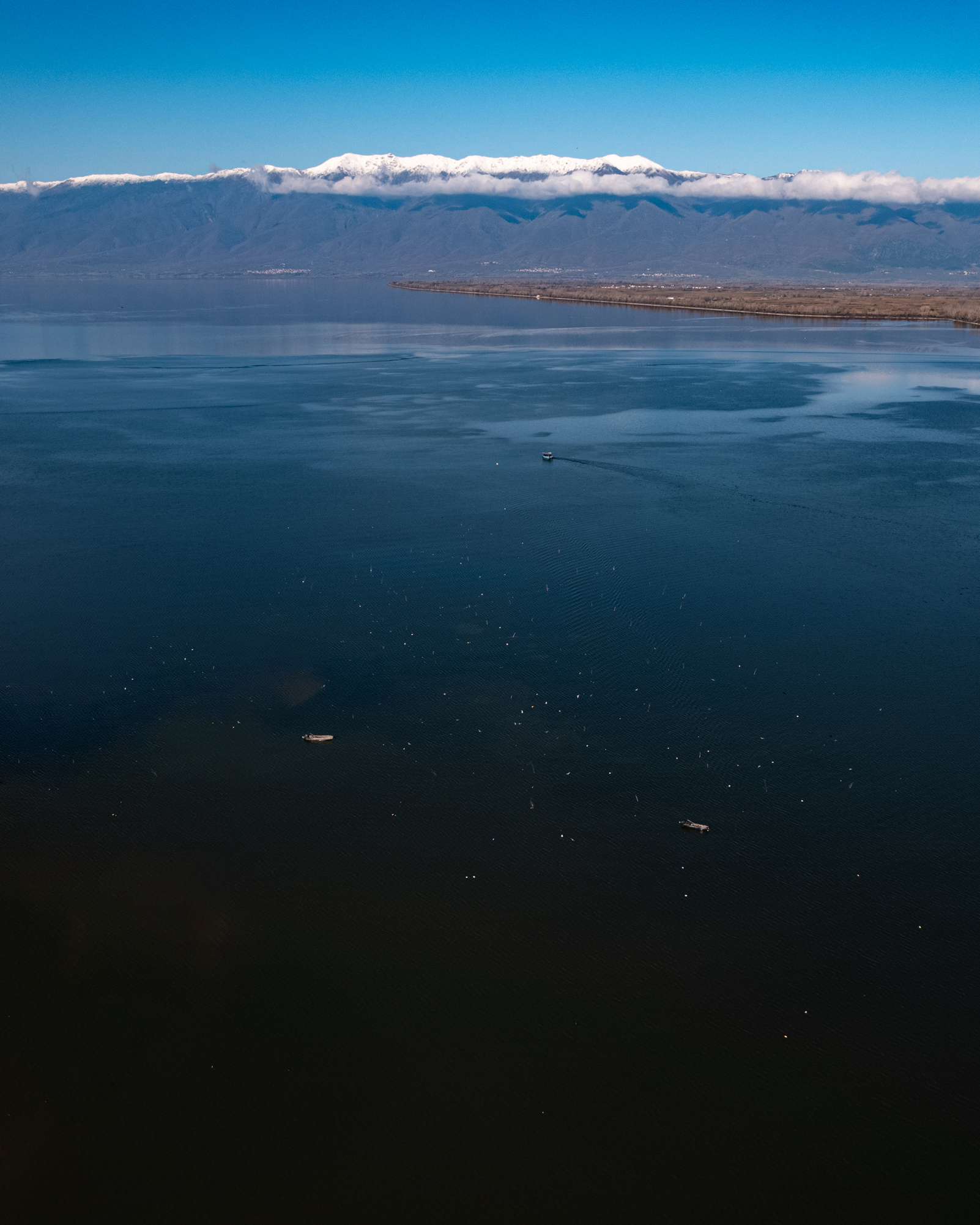 Aerial view across the blue waters of Lake Kerkini towards a snow-covered mountain range.