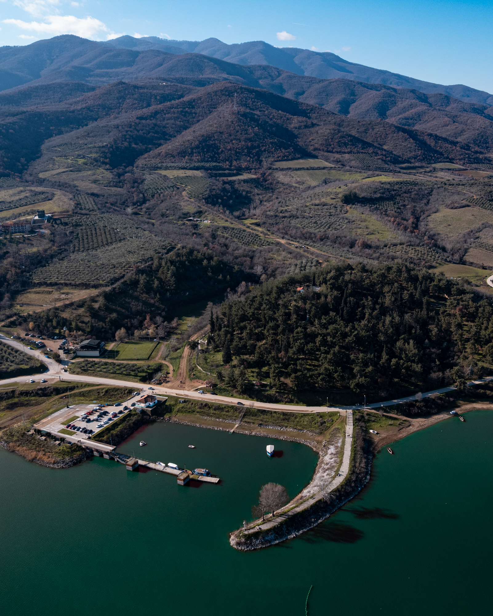 Aerial view of a small harbour and curved breakwater on Lake Kerkini, backed by wooded hills.