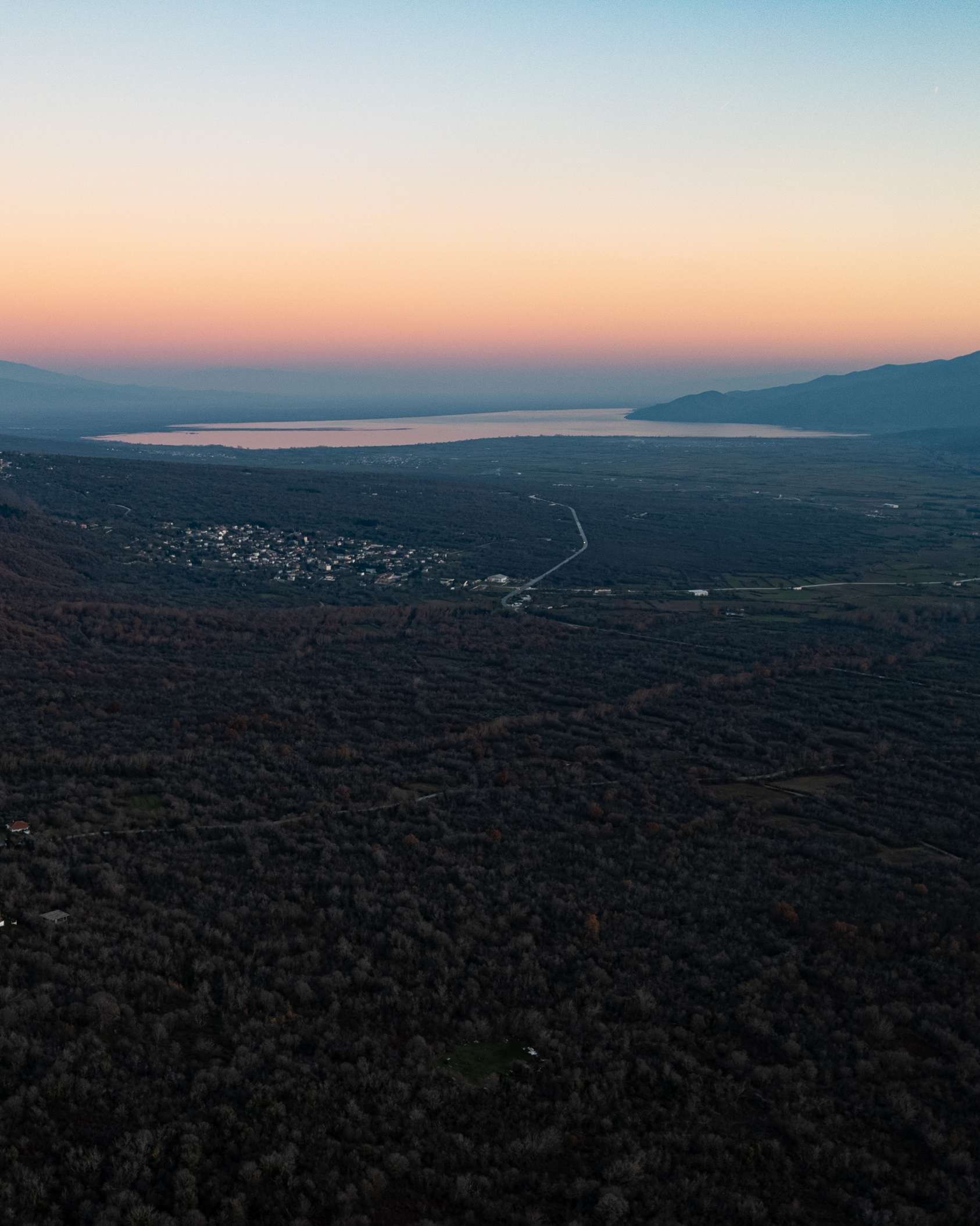 Aerial view of a village and Lake Kerkini in the distance beneath a peach-coloured evening sky.