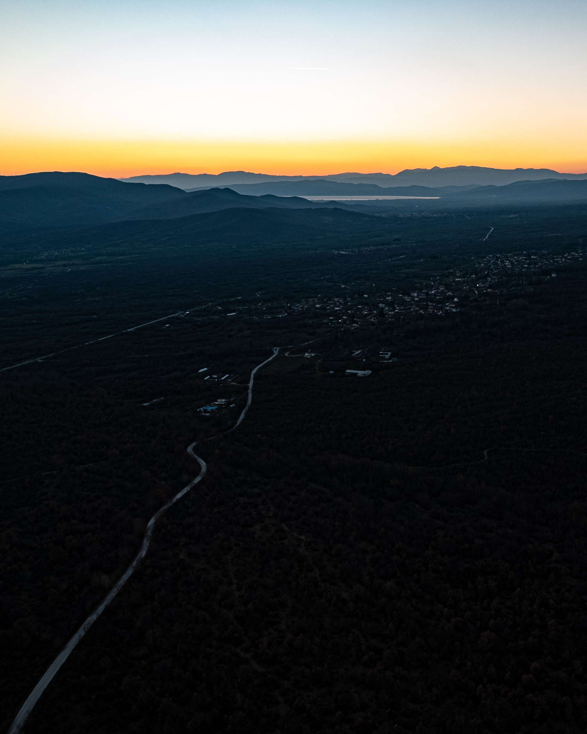 Aerial view of dark hills and winding roads beneath a yellow and blue evening sky.