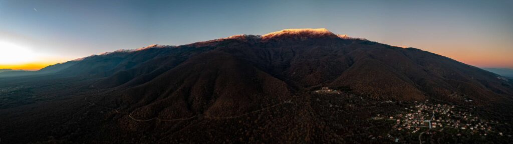 Panoramic aerial view of a mountain ridge and hillside villages beneath the fading light of sunset.