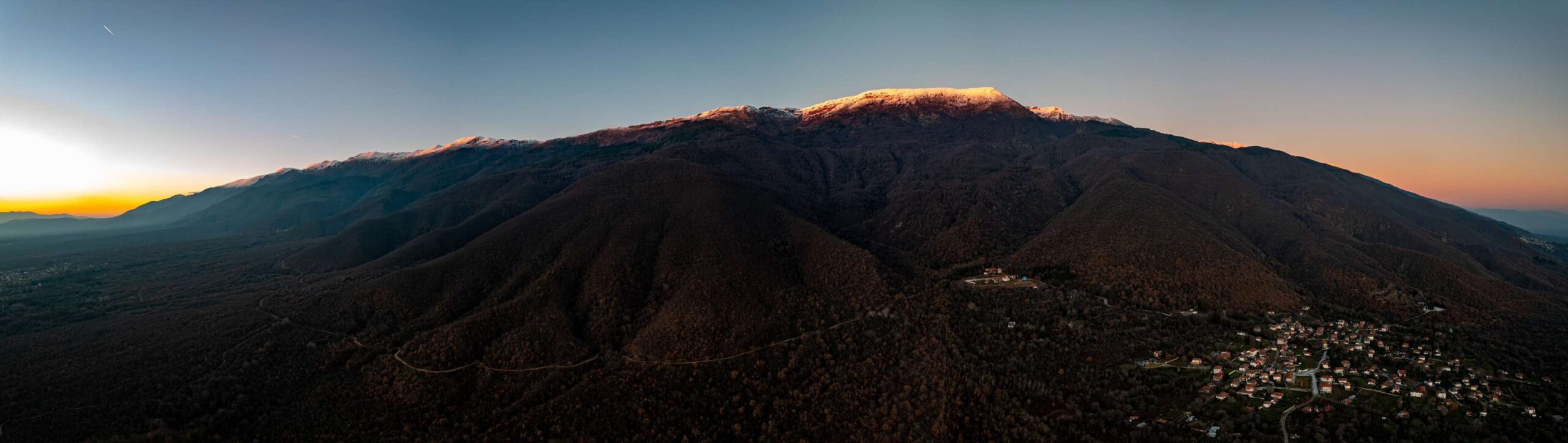 Panoramic aerial view of a mountain ridge and hillside villages beneath the fading light of sunset.