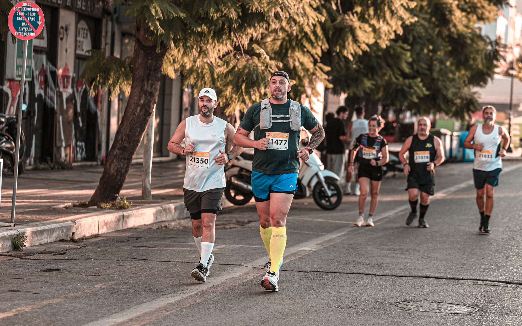 Paul and Iasonas running side by side along a tree-lined street during the Patras half marathon.