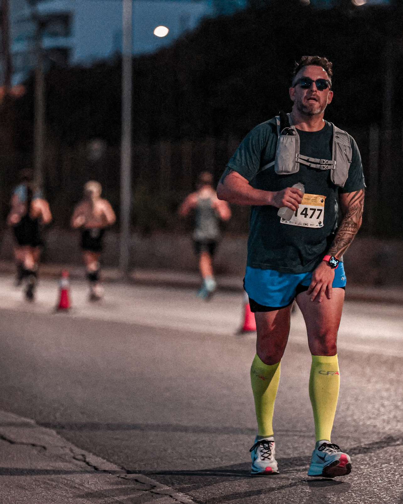 Paul running along the race course in blue shorts and yellow compression socks, with runners behind him.
