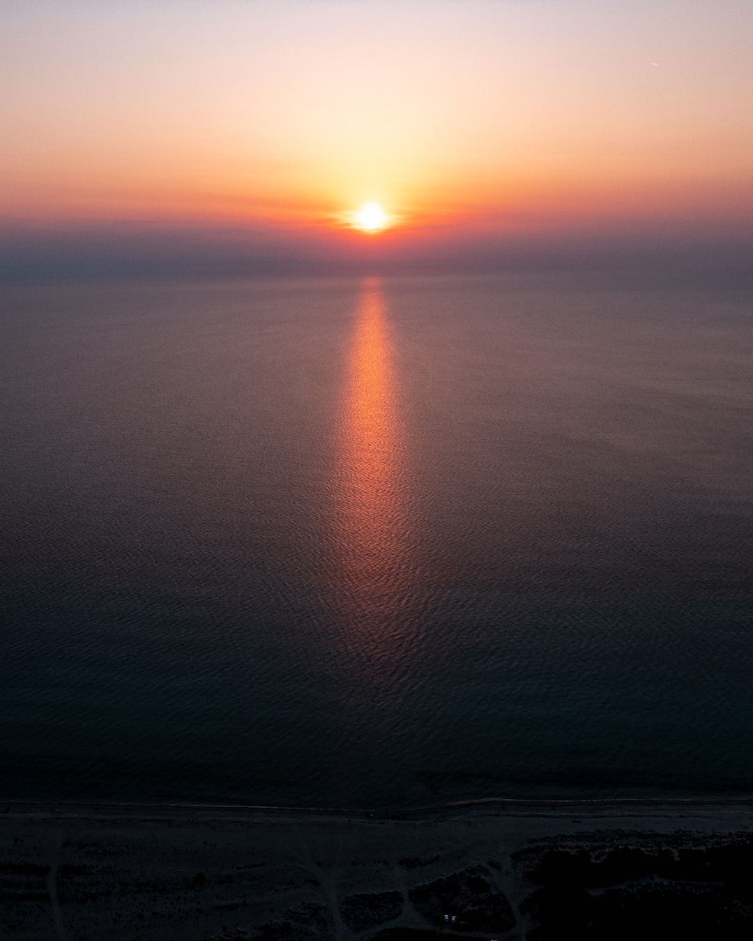Aerial view of the setting sun and its orange reflection across the sea at Possidi Cape.