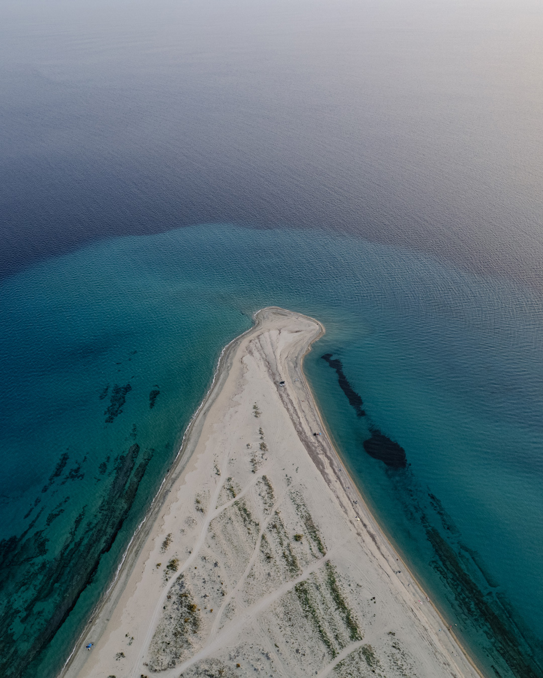 Aerial view along the narrow sand spit at Possidi Cape, with clear turquoise water on both sides.