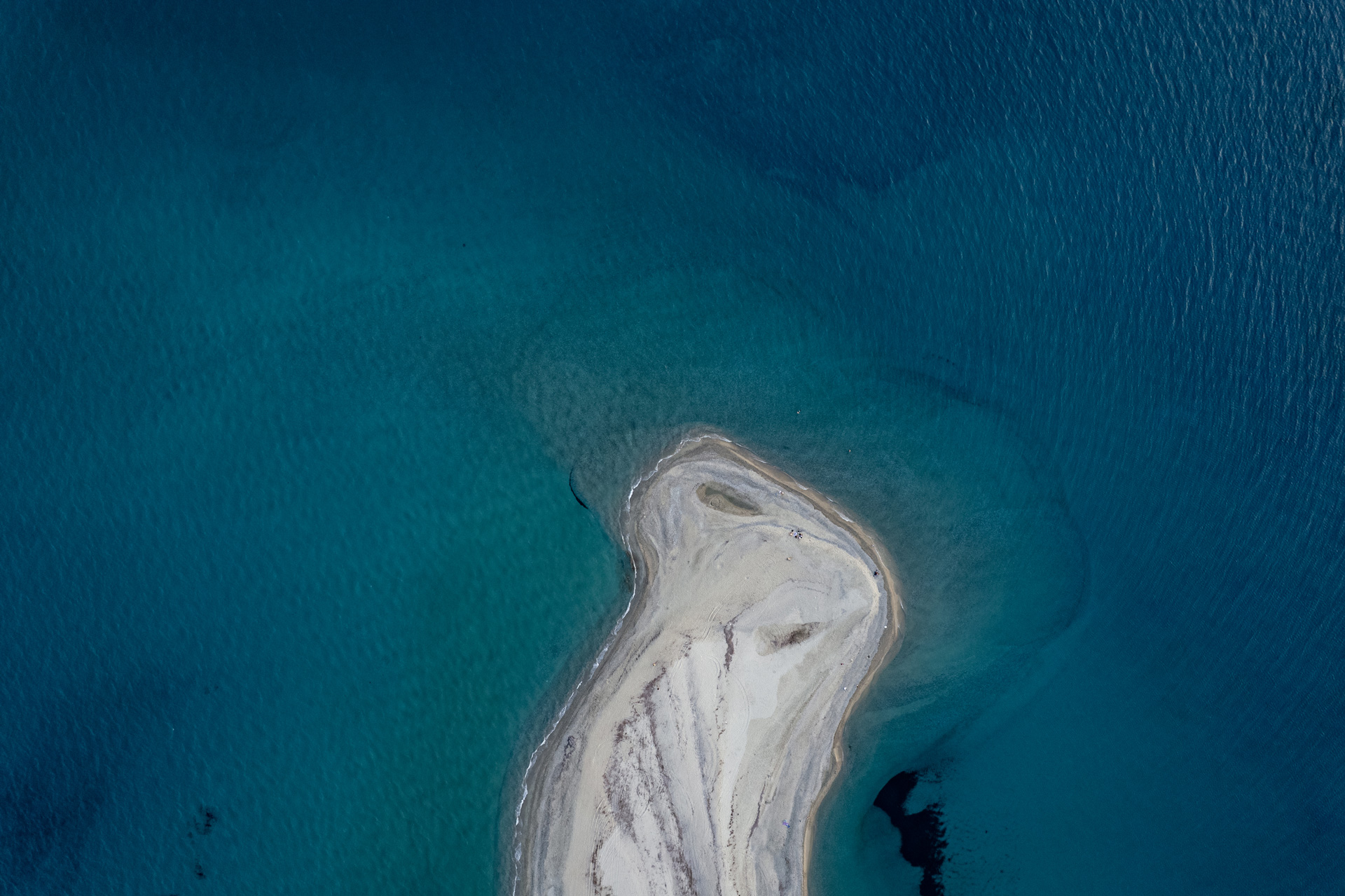 Overhead drone view of the curved white sand spit at Possidi Cape surrounded by turquoise water.