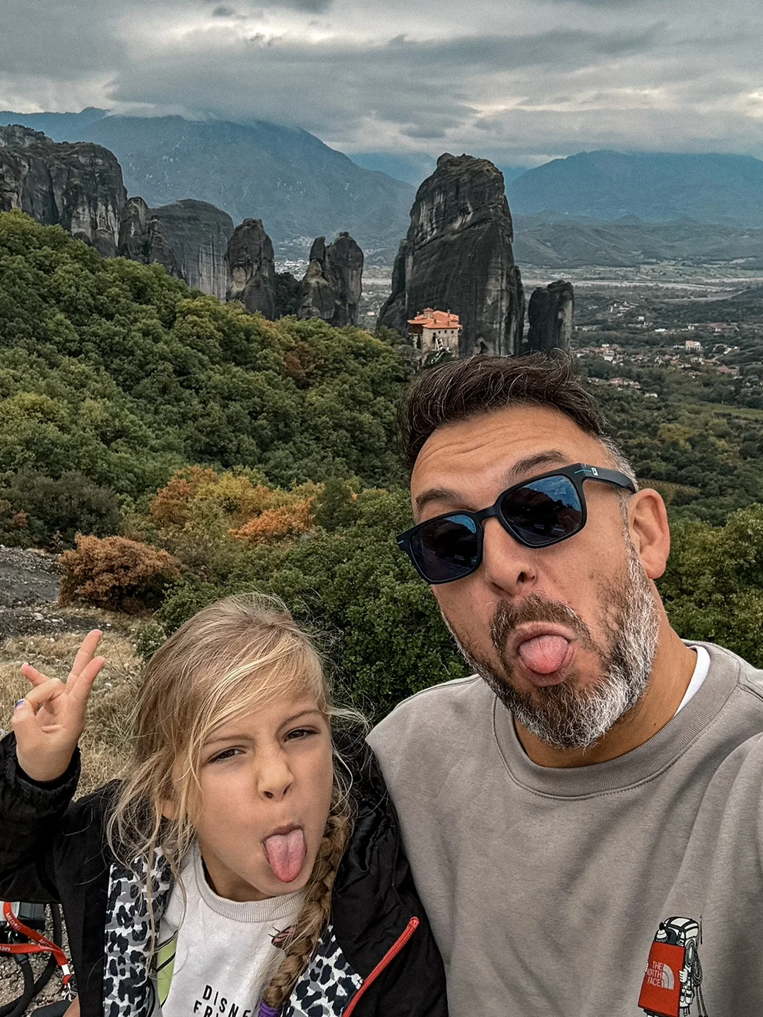 Polychronis and Melina pulling funny faces for a selfie, with the rocks of Meteora behind them.