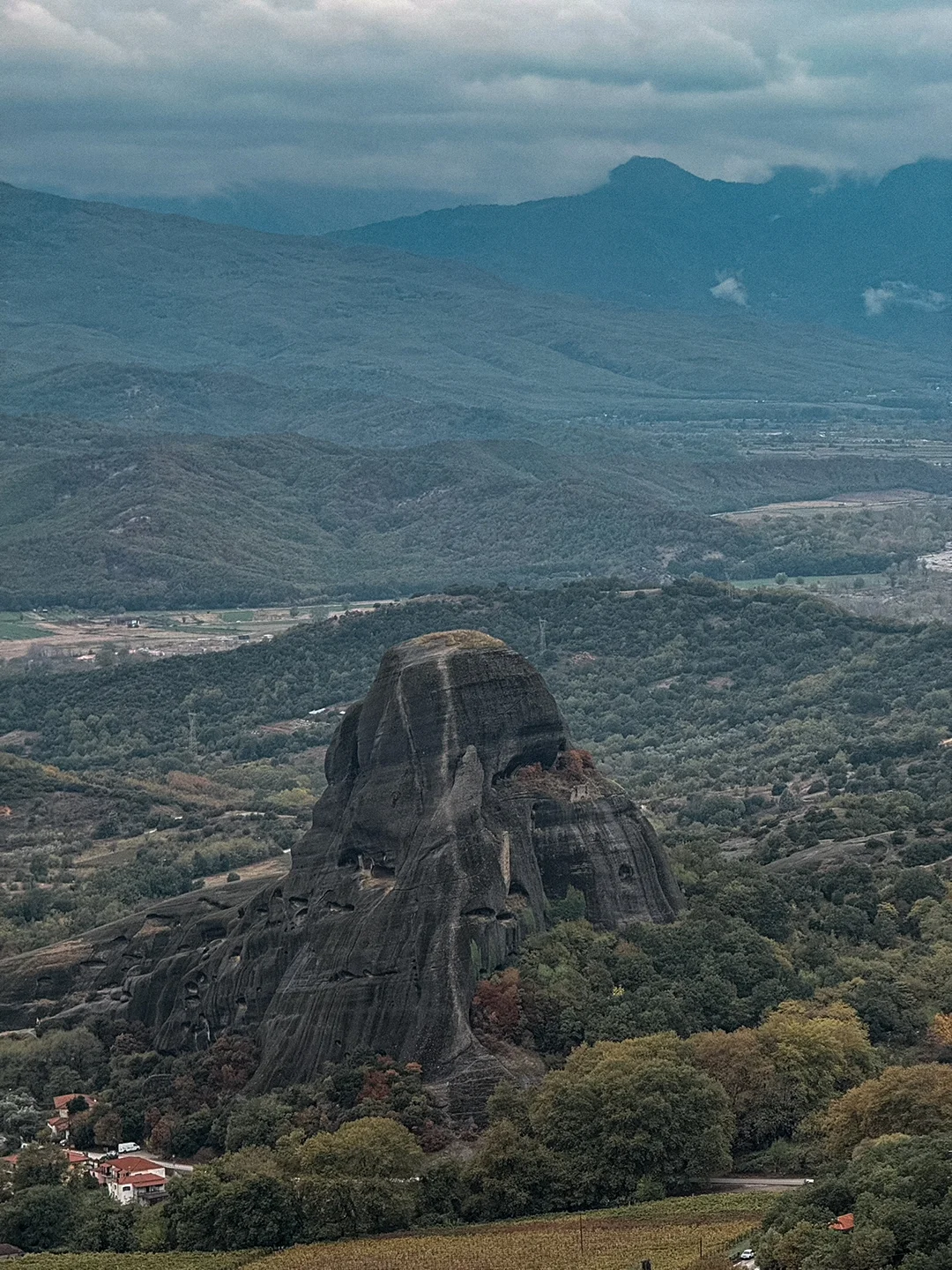 View across a solitary rock pillar and wooded slopes towards Kalampaka and distant mountains.