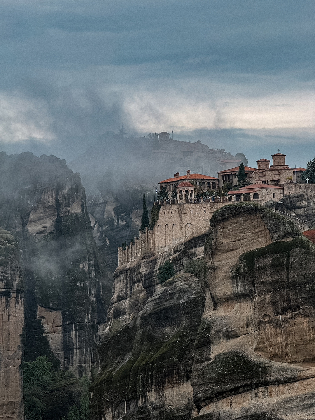 Clifftop monastery at Meteora overlooking a deep rocky gorge filled with mist.