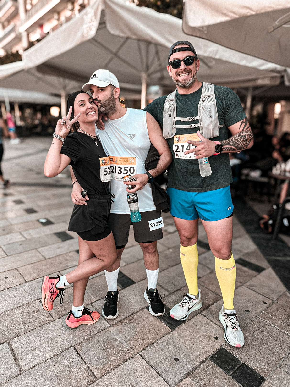 Three friends posing together in running clothes with their race medals in Patras.