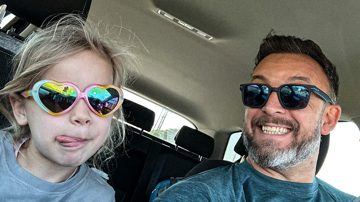 Paul and Melina smiling for a selfie in a car, both wearing sunglasses.