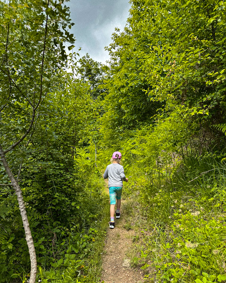 Melina standing on a narrow trail surrounded by dense green woodland in Ano Milia.