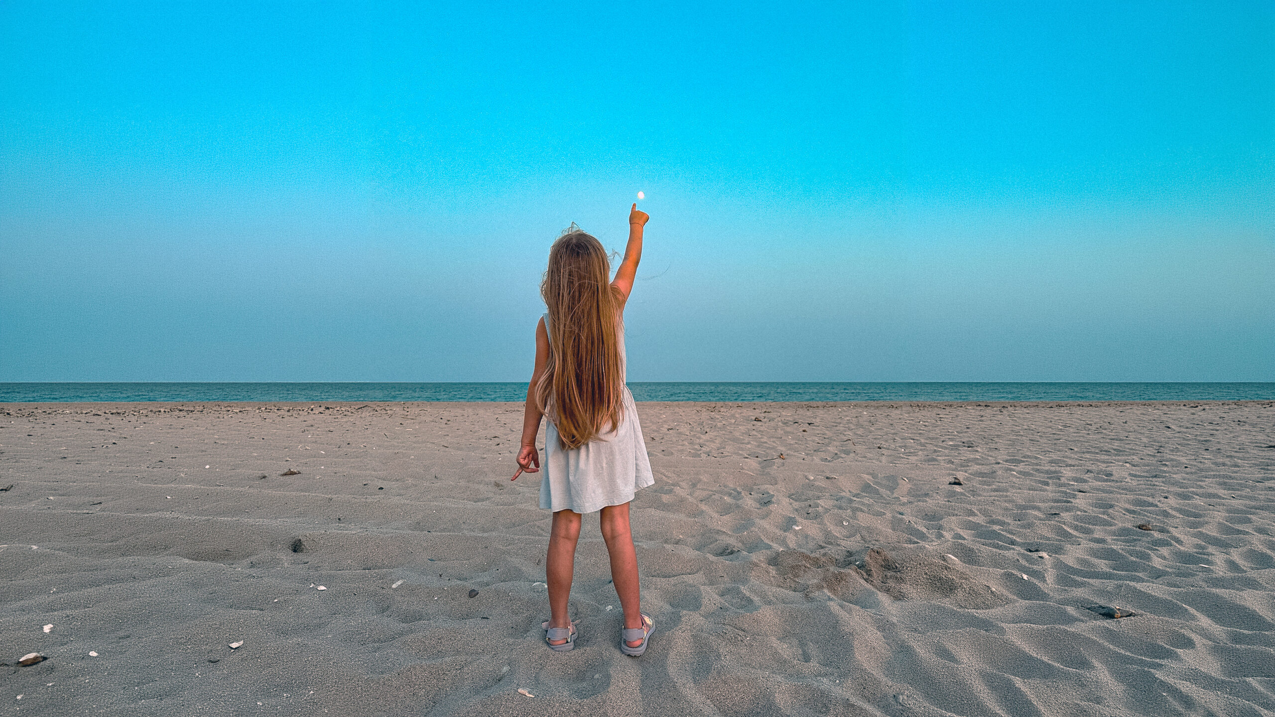 Eirini standing on the sand at Possidi Cape, raising her arm toward the blue evening sky.