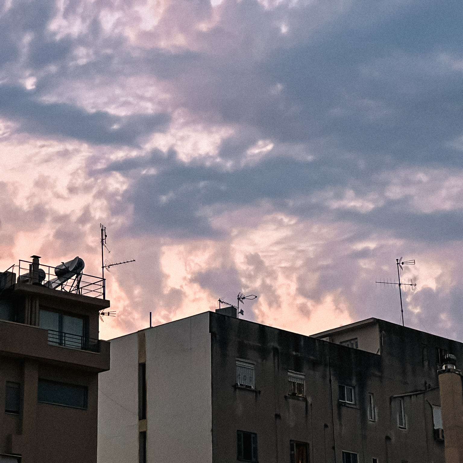 Pink and purple evening clouds above apartment rooftops and television aerials in Patras.