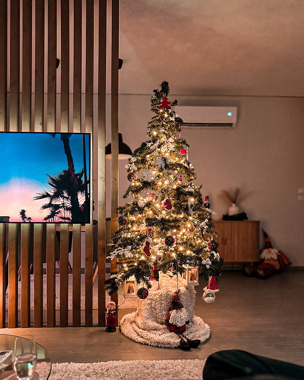 Decorated Christmas tree glowing beside a television and wooden room divider.
