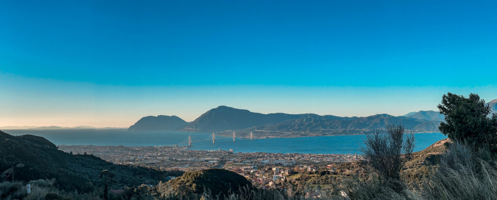 Panoramic view over Patras and the Rio–Antirrio Bridge, with blue water and mountains beyond.