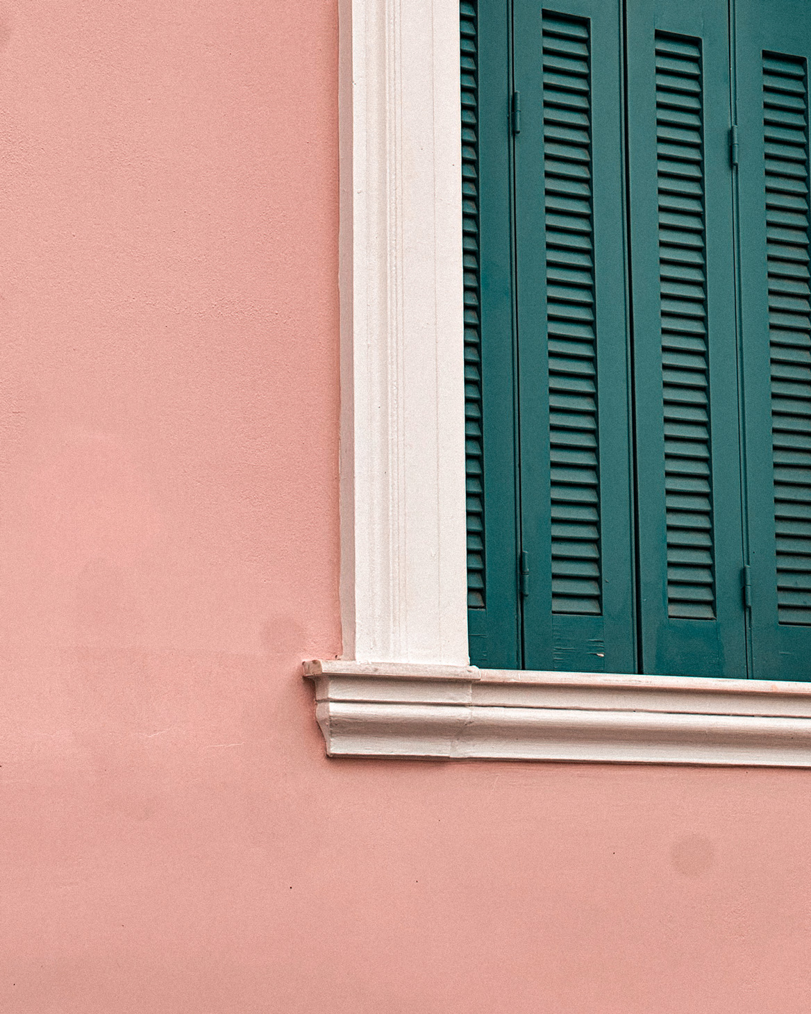 Dark green window shutters framed in white against a pink wall in Patras.