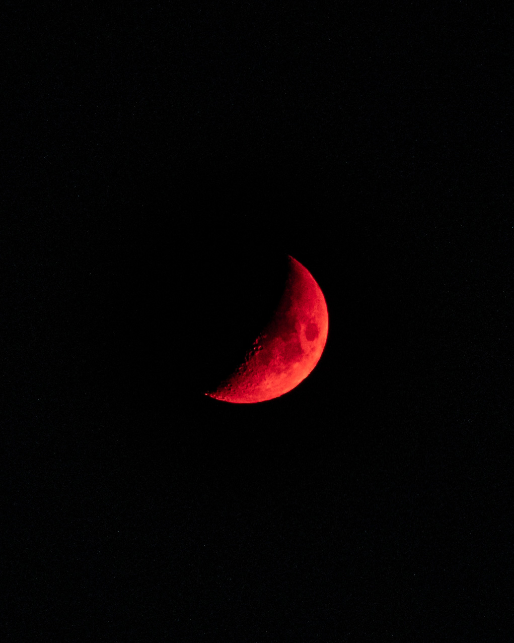 A red crescent moon against a black night sky.