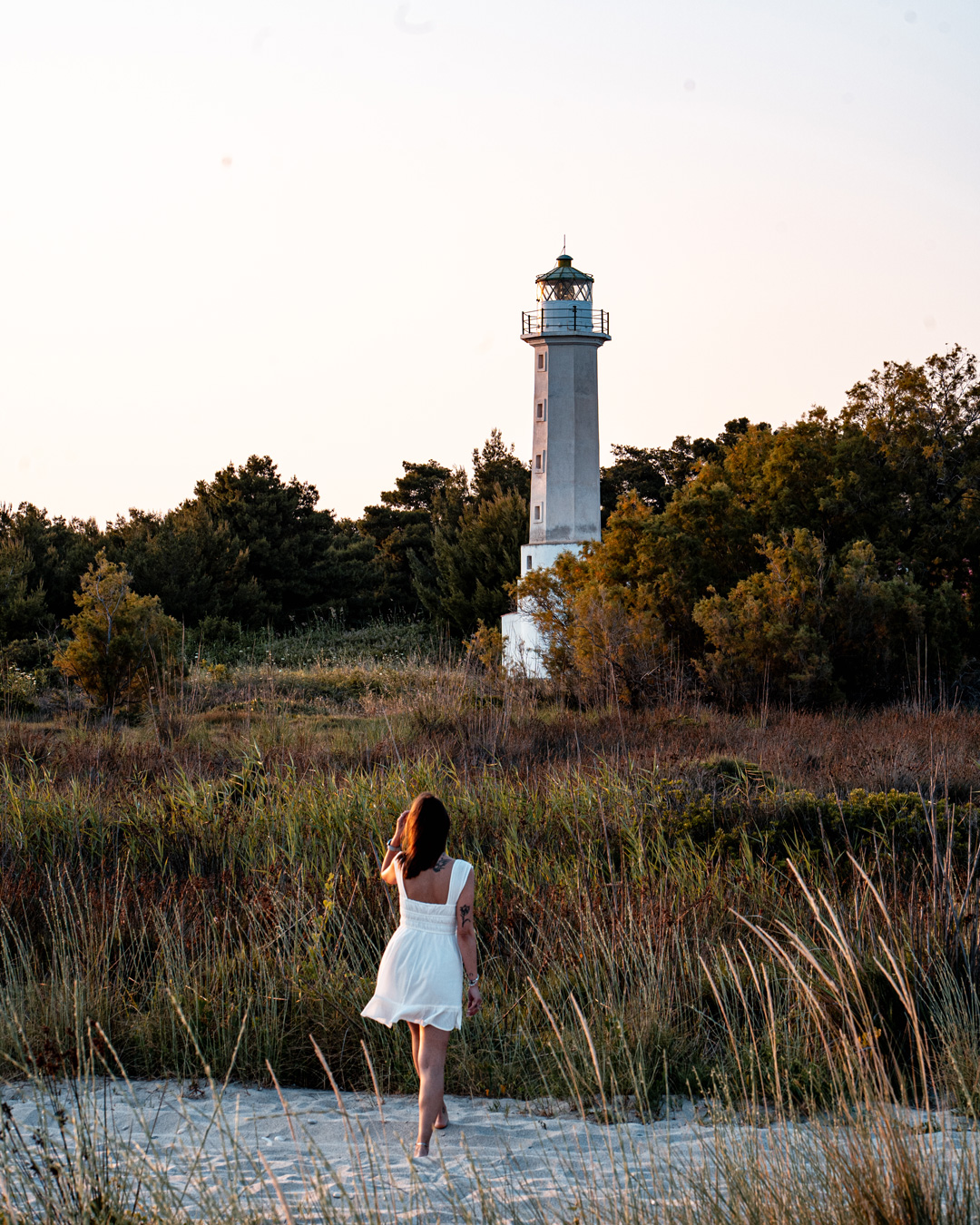 Melina standing among grasses below the white lighthouse at Possidi Cape.