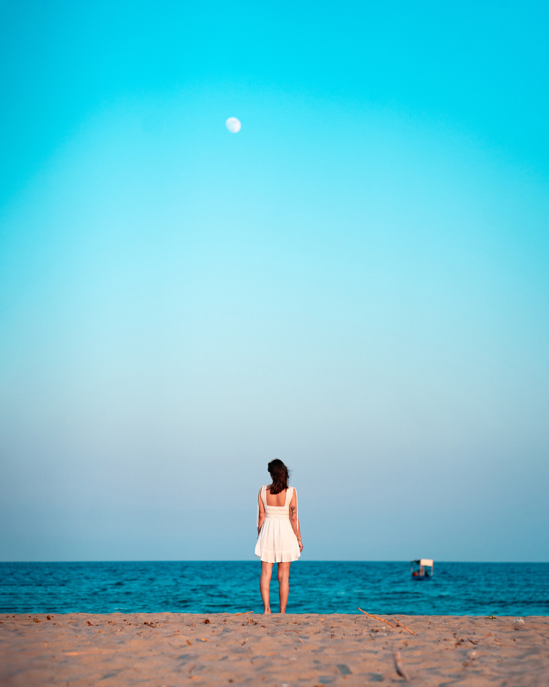Eirini standing by the sea beneath the moon, framed by a wide blue evening sky at Possidi Cape.