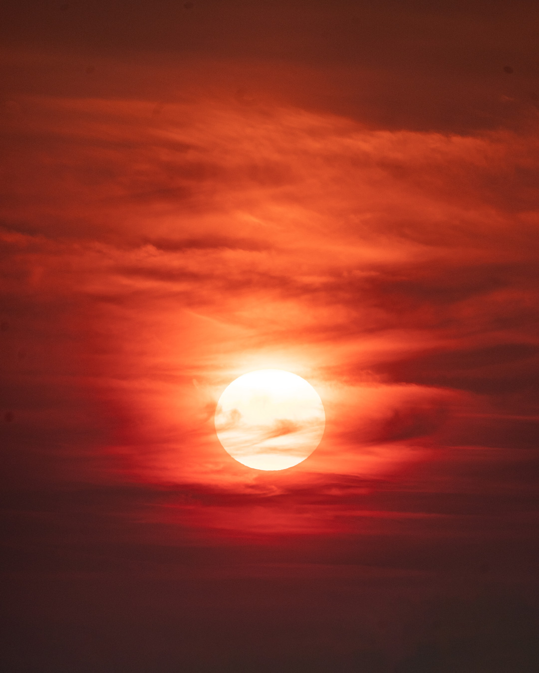 The orange sun shining through deep red clouds at sunset in Chalkidiki.
