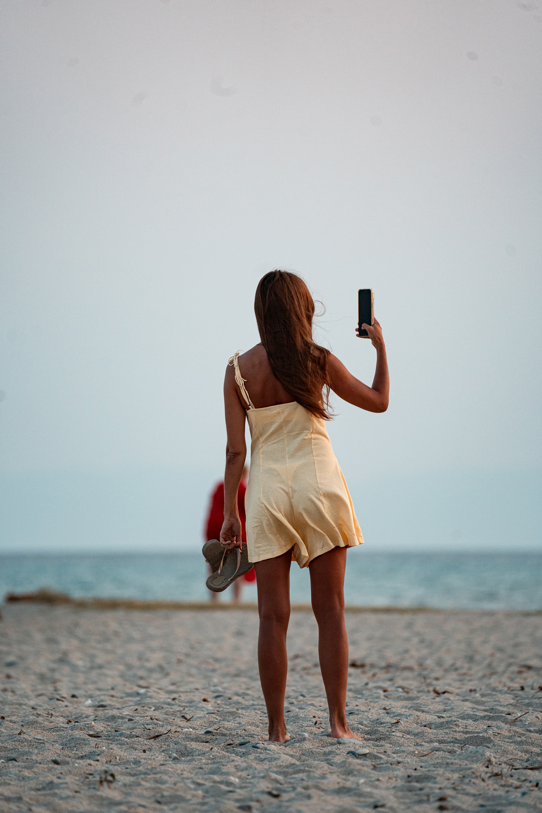 Eirini standing on the beach with her phone raised toward the evening sky.