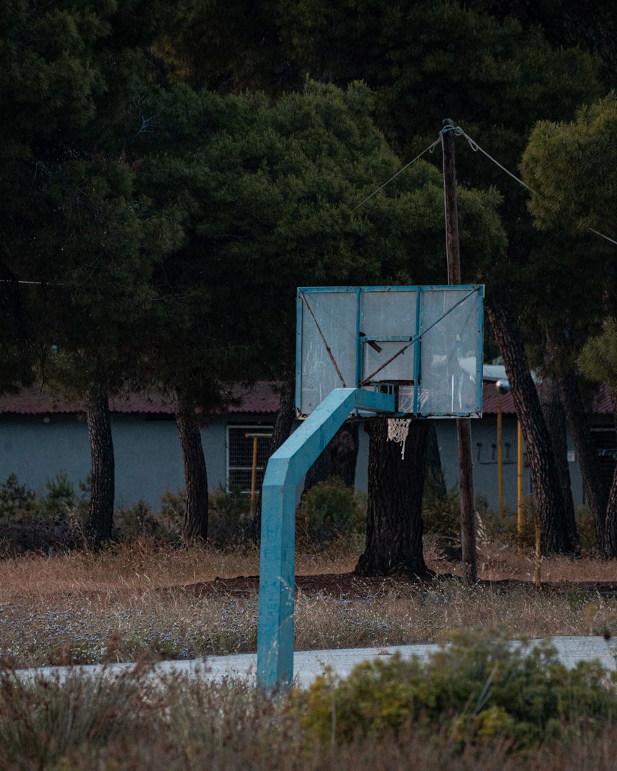 A weathered basketball hoop beside trees and an overgrown outdoor court in Chalkidiki.