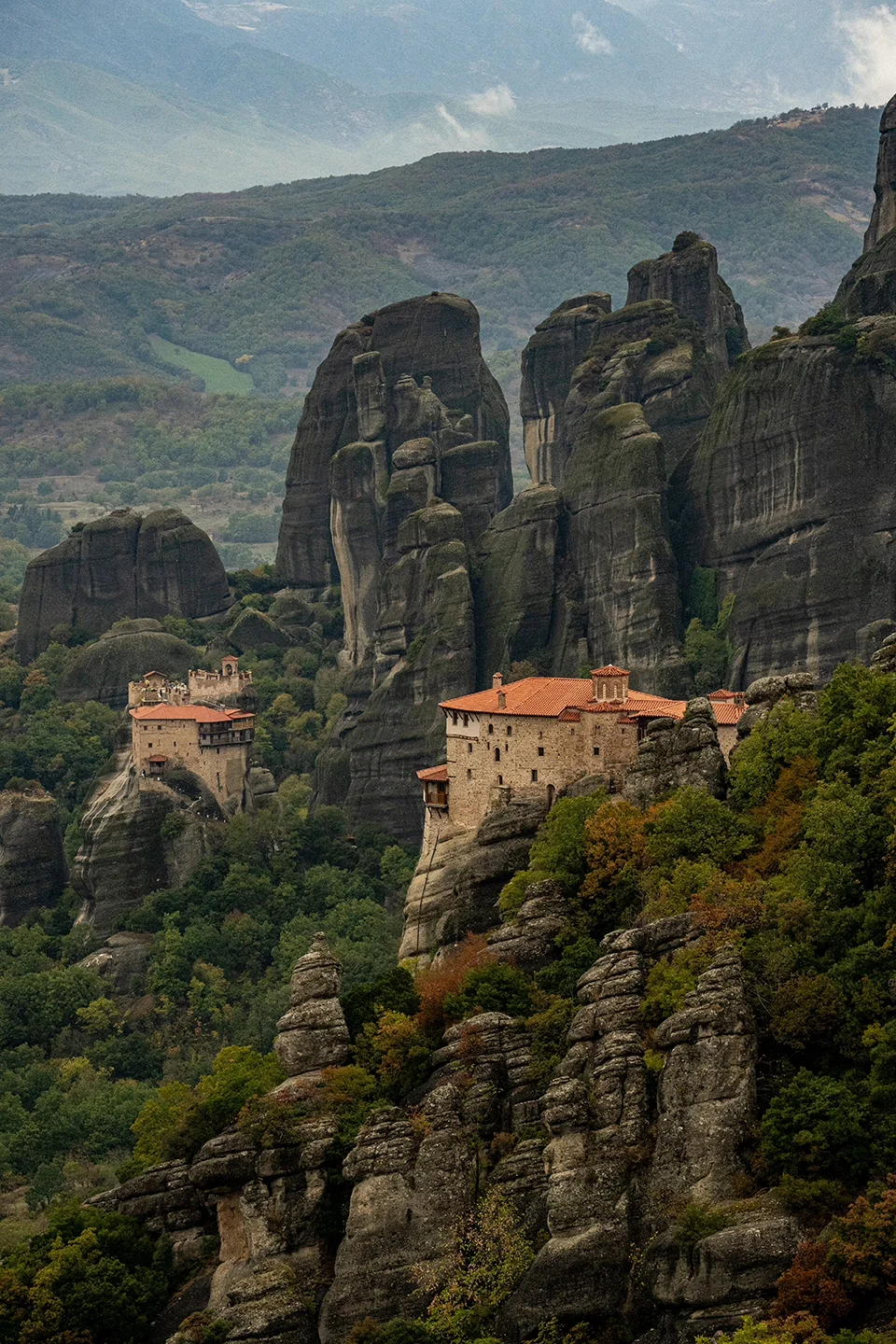 Terracotta-roofed monasteries nestled among tall rock pillars and autumn woodland at Meteora.