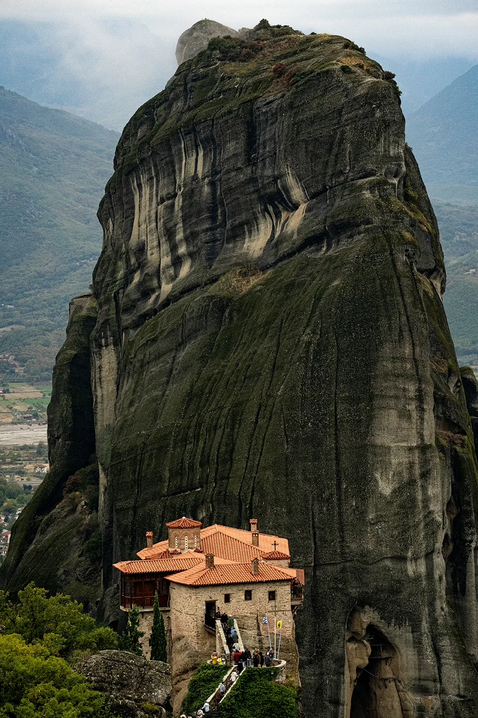 Small monastery with terracotta roofs beneath a towering rock pillar at Meteora.